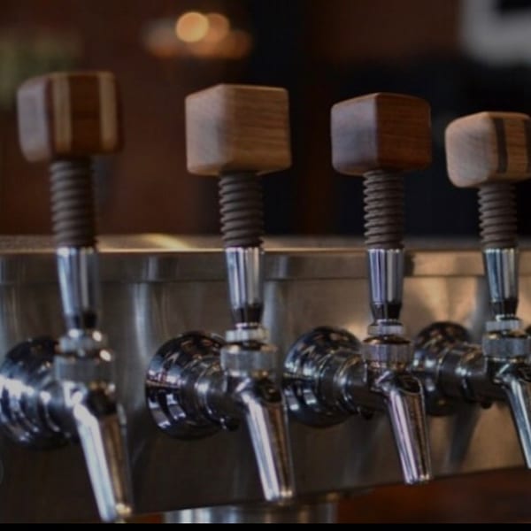 Four beer taps with wooden handles and chrome spouts, ready to pour craft ales.