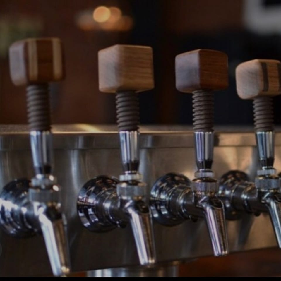 Four beer taps with wooden handles and chrome spouts, ready to pour craft ales.