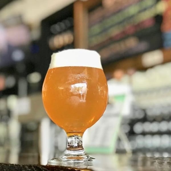 A glass of amber ale with a foamy head sits on a dark bar top at Underground Coffee and Ales.