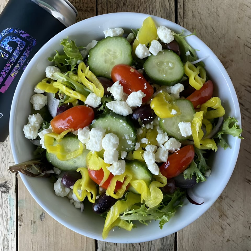 Overhead view of a vibrant Greek salad with lettuce, cucumbers, tomatoes, olives, peppers, and feta cheese.
