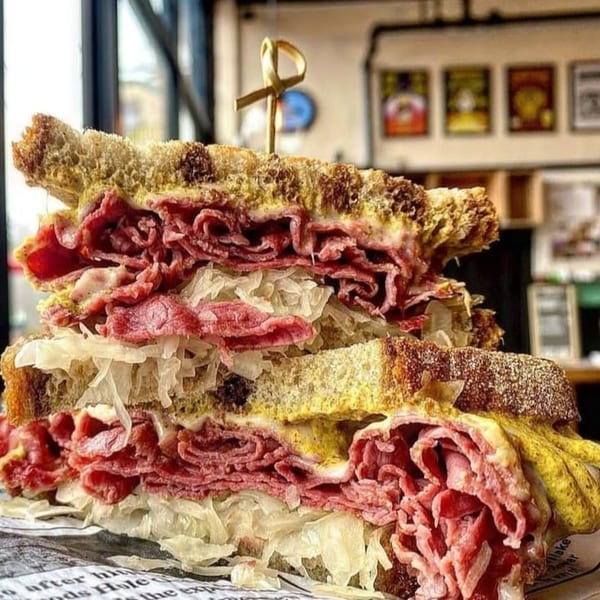 A towering pastrami and sauerkraut sandwich on rye bread with mustard, held together by a toothpick.